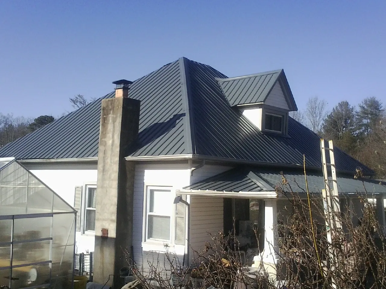 Dark blue standing seam metal roof on a white farmhouse with dormer — Slate & Tile Roof Repair by Roofing Brothers in Glenwood Landing