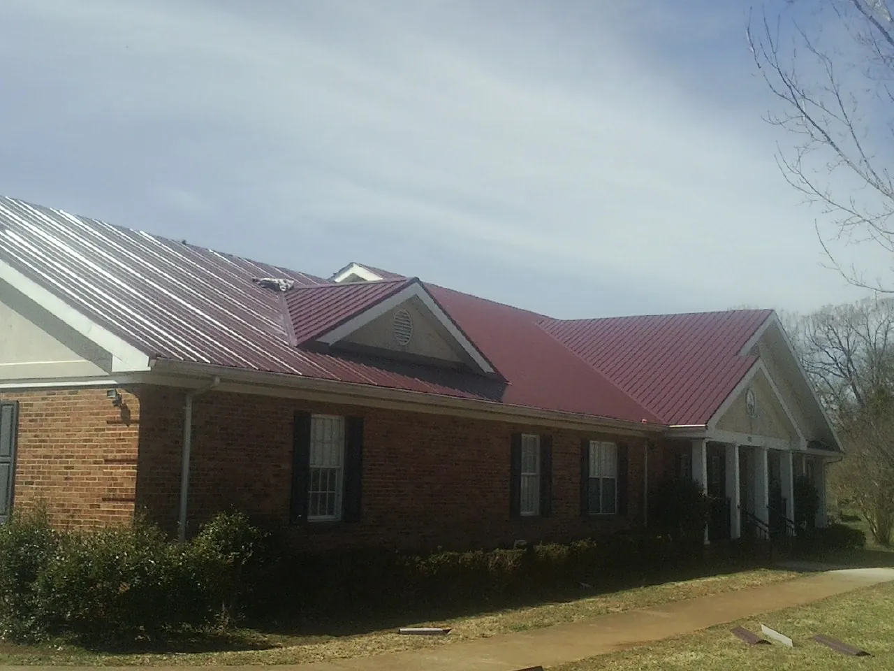 Red metal roof with gabled entries on a long brick building, from a Hail Damage Roof Repair job in Glenwood Landing