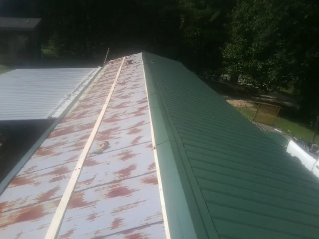 Old rusted panels beside newly installed green metal roofing — Wind Damage Roof Repair by Roofing Brothers in Glenwood Landing