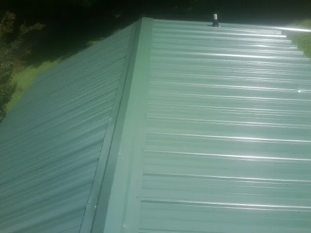 New green metal panels meeting at the ridge of a roof — Flat Roof Repair work by our crew in Glenwood Landing