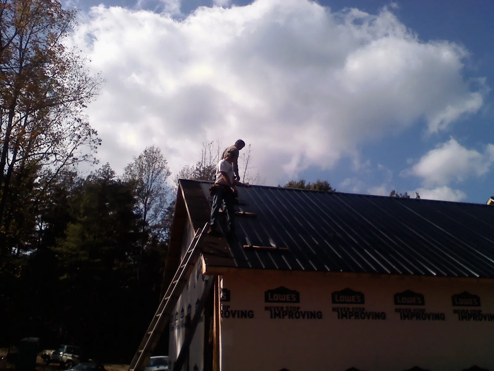 Roofer fastening dark metal panels high against a cloudy sky, from a Roof Inspection job in Glenwood Landing