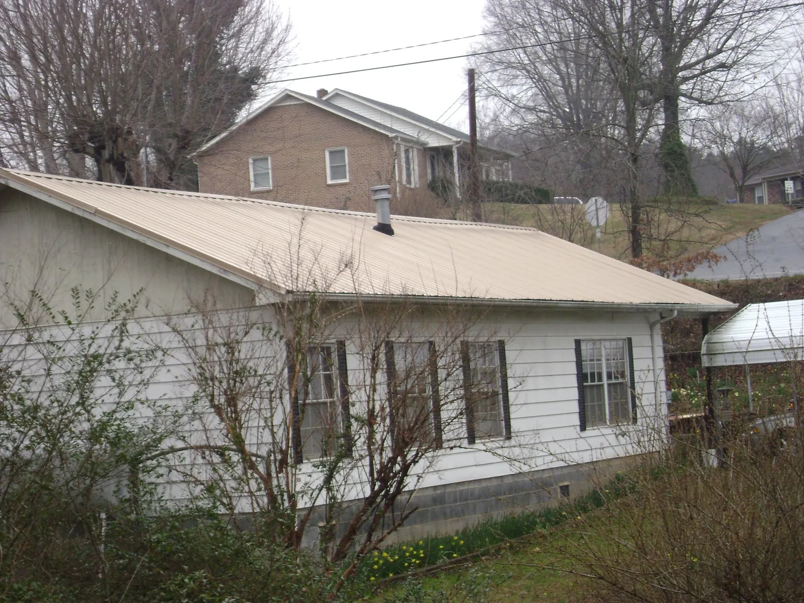 Tan metal roof on a white sided house set into a hillside — Commercial Roofing by Roofing Brothers in Glenwood Landing
