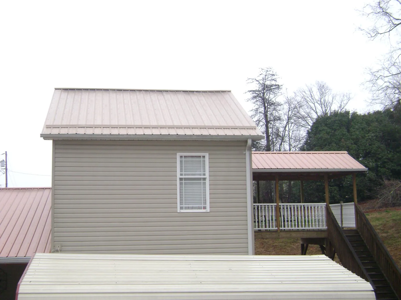 Tan metal roofs on a two story addition and attached porch, from a Roof Replacement job in Glenwood Landing