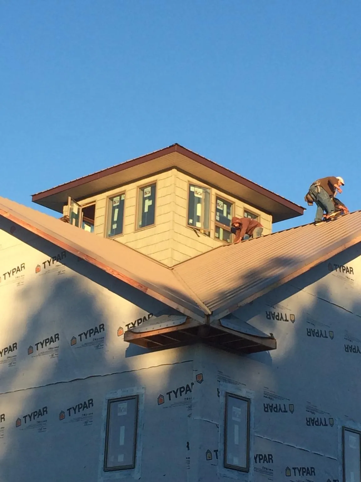 Roofers working around a rooftop cupola on a new metal roof at sunset — Roof Waterproofing in Glenwood Landing by Roofing Brothers